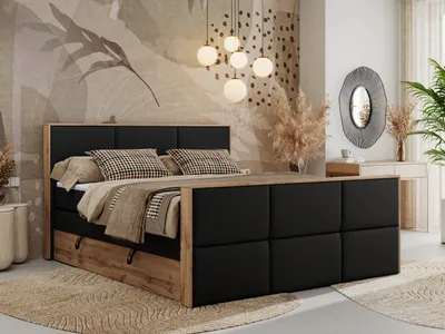 A bedroom scene featuring a bed with storage, pillows, and blankets, set against a decorative wallpaper and a dressing table with a mirror.