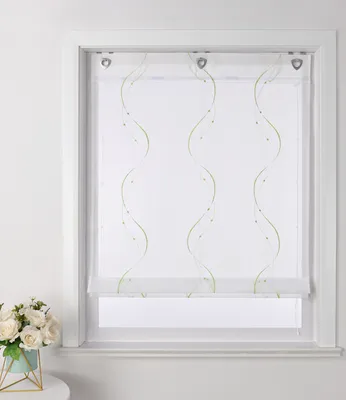 A white window frame with a sheer white roller blind featuring green wavy embroidered lines and small green beads.