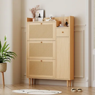 A light wood shoe cabinet with rattan doors and a drawer, placed in a room with a plant and a rug.