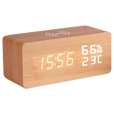A digital alarm clock made of wood with a wireless charging pad on top.