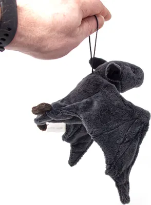A hand holding a plush toy bat by a string.