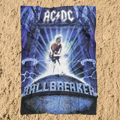 A blanket with AC/DC's Ballbreaker album art is laid out on a sandy surface.