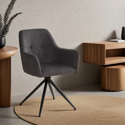 A gray corduroy armchair with a black metal base is placed on a round beige rug in a room with a textured wall and wooden furniture.