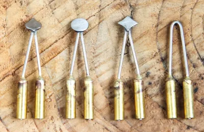 A set of five different metal tips for a wood-burning tool, laid out on a wooden surface.