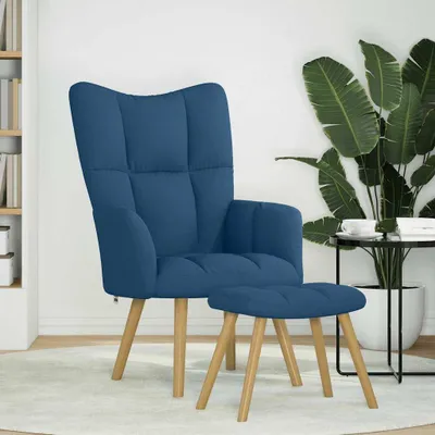 A blue fabric armchair and matching ottoman are placed on a light-colored rug in a room with a bookshelf and a large potted plant.