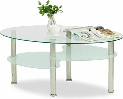 A glass coffee table with a metal frame, a vase with greenery, a cup and saucer, and a magazine on top.
