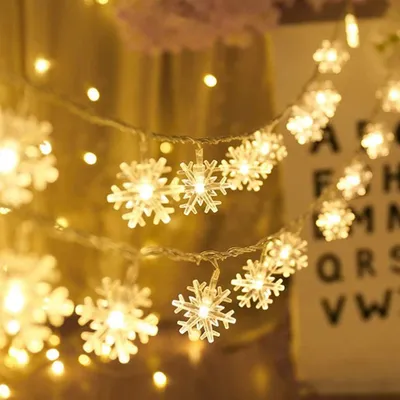 A close-up of snowflake-shaped LED string lights, glowing warmly.