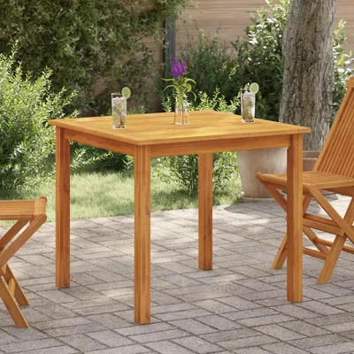 A wooden table and chairs set up on a patio with greenery in the background.