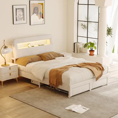 A bedroom scene featuring a bed with storage drawers and a lit headboard, bedside tables, and artwork on the wall.
