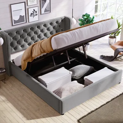 A grey upholstered bed with its storage compartment open, revealing storage boxes and pillows inside.