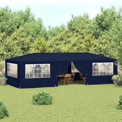 A navy blue party tent set up in a grassy backyard with trees in the background. There is outdoor furniture inside the tent.