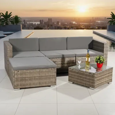 A rattan sofa set with grey cushions is placed on a tiled patio overlooking a city skyline at sunset.