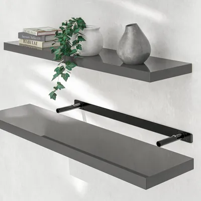 Two gray shelves mounted on a light gray wall. The top shelf has books, a plant, and a vase. The bottom shelf has a black bracket attached.