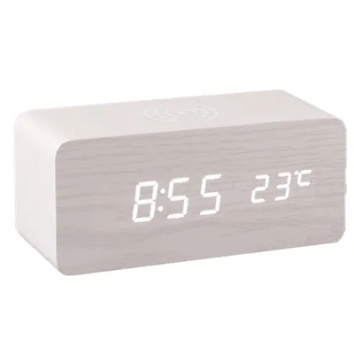 A digital alarm clock with a wood-grain finish and a wireless charging pad on top.