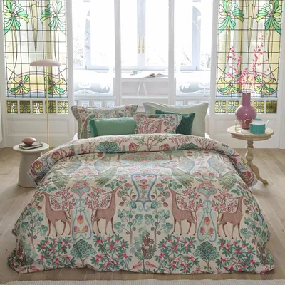 A bedroom scene with a bed dressed in a patterned duvet cover, pillows, and curtains.