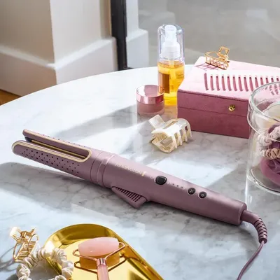 A curling iron and other beauty products are arranged on a marble table.