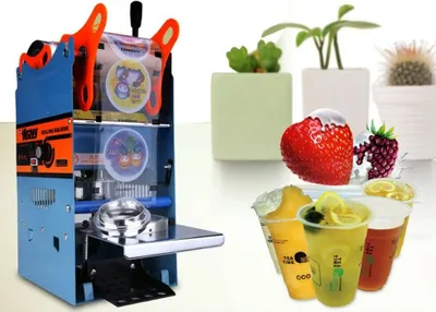 A product shot of a cup sealing machine next to drinks and decorative plants.