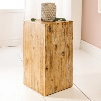 A wooden pedestal table with a decorative vase and leaves on top, placed on a white floor near a window and a pink wall.