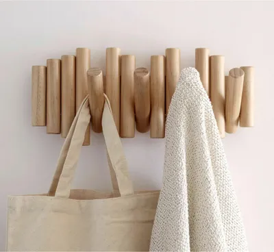 A wooden coat rack with hooks mounted on a white wall, holding a tote bag and a textured blanket.