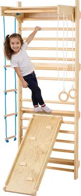A young girl is playing on a wooden gym set indoors.