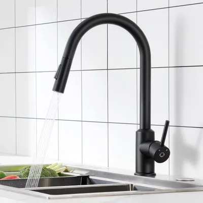 A black kitchen faucet with water running into a sink with vegetables.