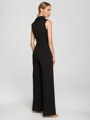A woman is posing in a black jumpsuit against a white background.