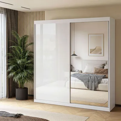 A modern bedroom with a large white sliding door wardrobe with mirrored doors, reflecting a bed and a framed picture on the wall. A large potted plant is placed next to the wardrobe.