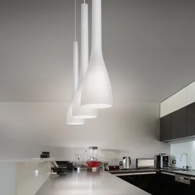 A modern kitchen with sleek countertops and cabinets, featuring three white pendant lights hanging from the ceiling.