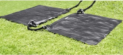 Two black solar mats are laid out on a green grassy lawn, connected by hoses.