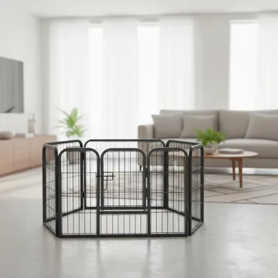 A black metal pet playpen is set up in a modern living room with a sofa and coffee table in the background.