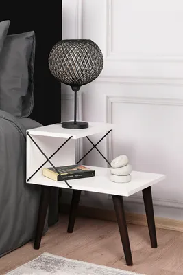 A bedside table with a lamp, book, and decorative stones next to a bed.