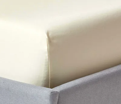 A close-up view of a cream-colored fitted sheet and a gray bed skirt.