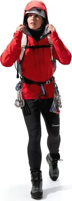 Dame in roter Mtn Guide Alpine Pro Jacke von Berghaus; ausgestattet mit Kletterausrüstung und Helm; bereit zum Bergsteigen.