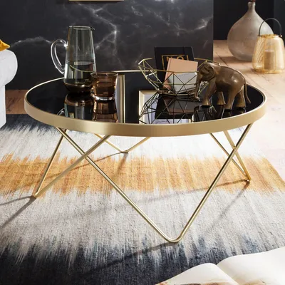 A modern coffee table with a black glass top and gold metal legs, set on a patterned rug in a living room.