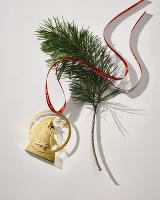 A gold-colored Christmas ornament shaped like a snow globe with a pine branch and red ribbon on a white background.