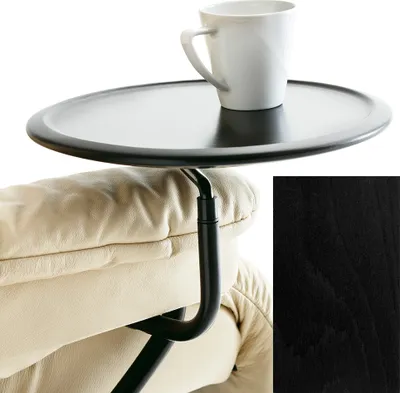 A black tray table is attached to the armrest of a beige leather armchair, with a white mug on the tray.