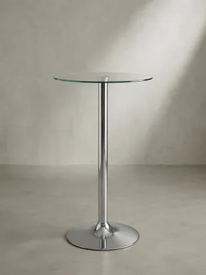Dreiviertelansicht des runden Bartisches, die die filigranen Proportionen zwischen der schlanken Mittelsäule und der 60 cm messenden Klarglasplatte perfekt in Szene setzt._#sku_BARSPM3.054#