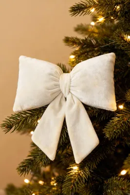 A cream-colored velvet bow is attached to a decorated Christmas tree branch.