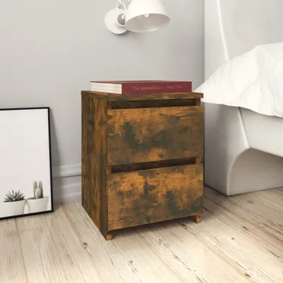 A bedside table with two drawers is placed next to a bed in a bedroom. A framed picture with plants is on the left, and a wall lamp is above the table.