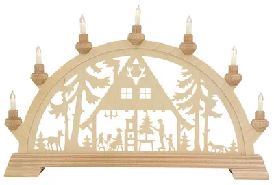 Ein traditioneller Schwibbogen aus Holz zeigt eine winterliche Szene mit einem Haus im Wald umgeben von Tannenbäumen und Tieren beleuchtet von neun kleinen Kerzen die auf dem Bogen verteilt sind