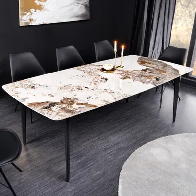A modern dining table with a marble-like top and black legs, set in a dining room with black chairs and a painting on the wall.