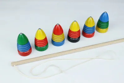 Six colorful spinning tops and a wooden stick with a string, arranged on a white background.