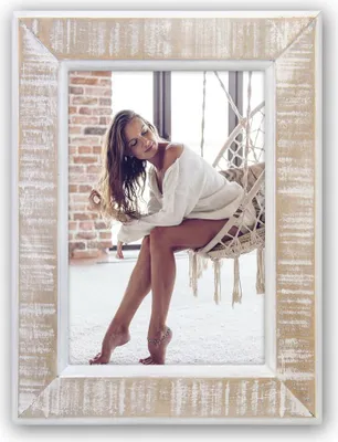 A woman sits in a hanging chair in a room with brick walls and a white carpet.
