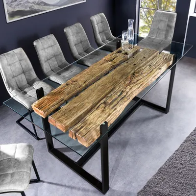 A dining room scene with a glass-top dining table featuring a rustic wooden centerpiece, surrounded by gray upholstered chairs.