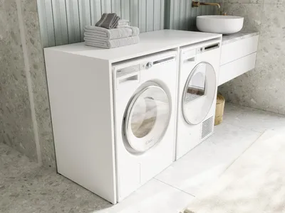 A modern laundry room with a white washing machine and dryer stacked on top of each other, with towels neatly folded on top of the cabinet.