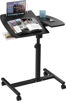 A black adjustable laptop table with wheels, a tablet, a book, a cup, and a phone on it, set against a white background.