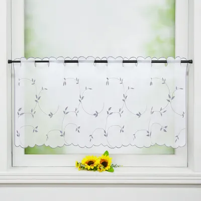 A white sheer curtain with a delicate gray leaf embroidery pattern hangs on a window rod. Two small sunflowers are placed on the windowsill below the curtain.
