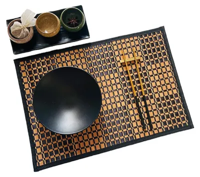 A table setting with a bamboo placemat, a black bowl, chopsticks, and small dishes with tea bags and spices.