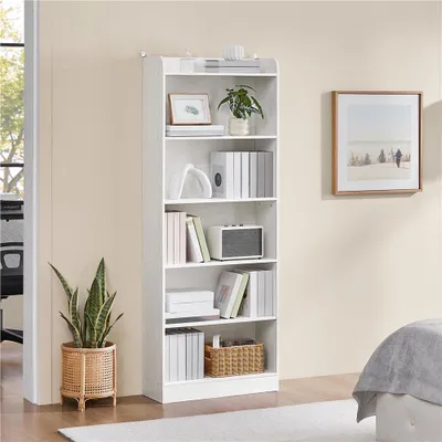 A white bookshelf filled with books and decorative items, placed next to a potted plant and a framed picture on the wall.