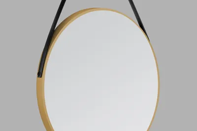 A round mirror with a gold frame and a black leather-look strap hanging against a plain gray background.